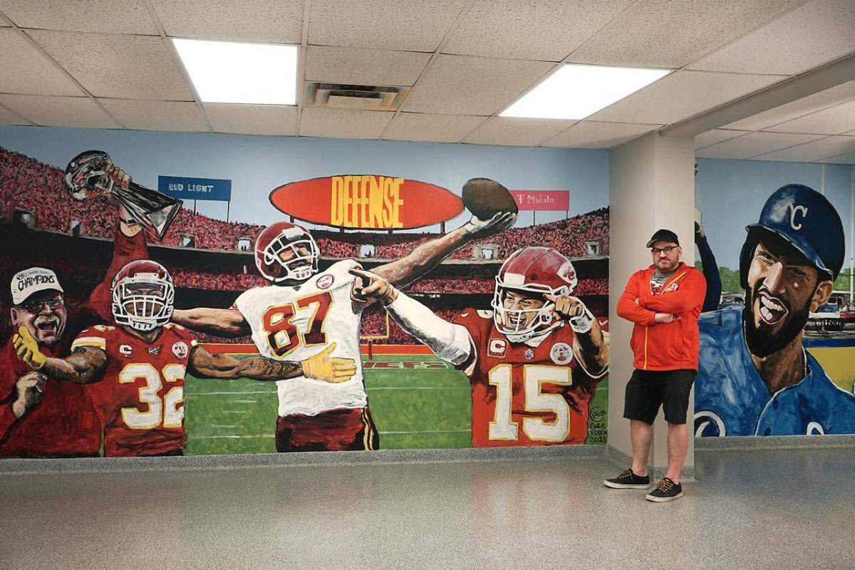 Chris Fleck standing beside the Chiefs mural he created for Specialty Industries